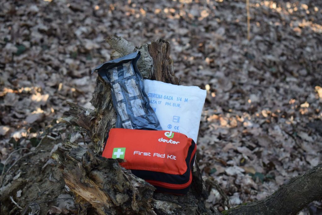 A first aid kit, Israeli bandage and sterile gauze laid out on a tree stump surrounded by Autumn leaves on a sunny afternoon