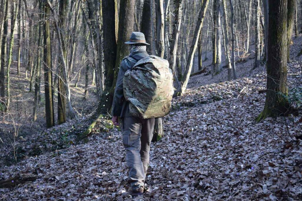 A man walking in the forest, carrying a haversack with a camo bag cover