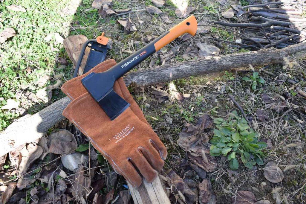 The 5 Best Survival Axes, Fiskars X10 laying on a pair of leather work gloves on a log in the wood on a sunny day