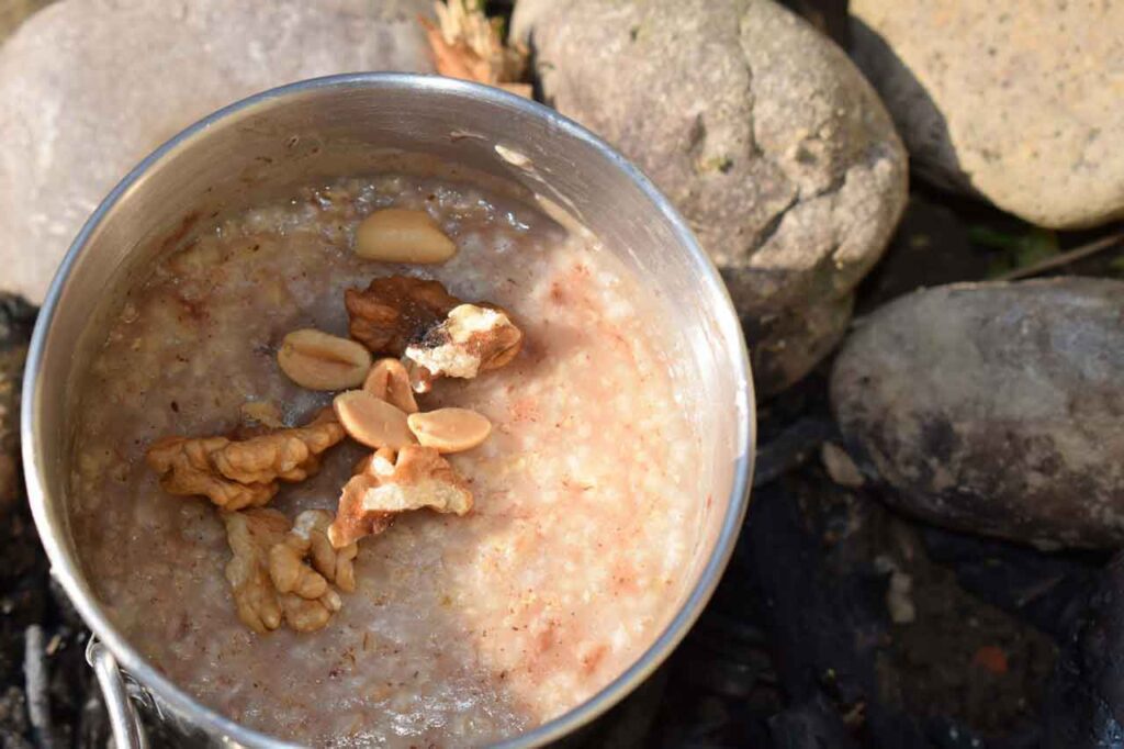 Oats with walnuts and cinnamon in a stainless steel cup cooking over a camp fire