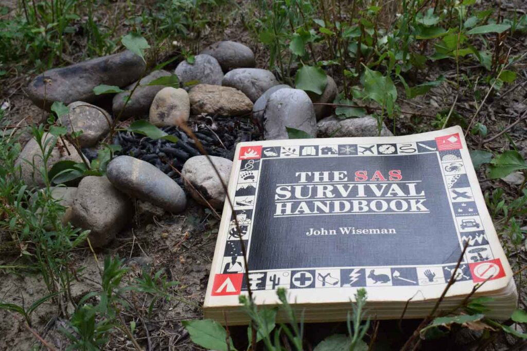 The SAS Survival handbook laying beside a campfire that has been put out