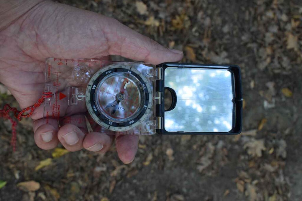 A Mans Hand Holding A Suunto MC2 Compass Surrounded By Dead Leaves